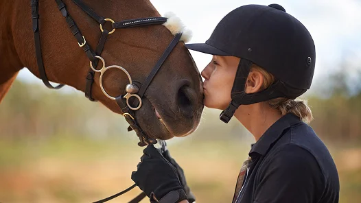 Gros plan d'un jockey embrassant doucement un cheval sur le nez, capturant le lien entre le cavalier et le cheval dans le sport équestre.